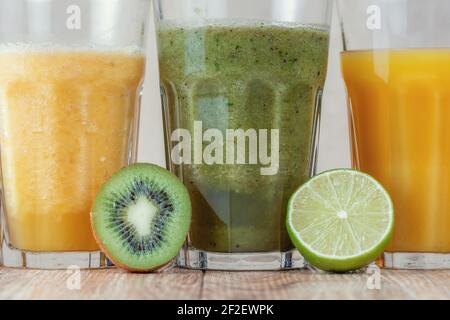 Trois grands verres avec des smoothies aux kiwis et aux épinards dans une rangée entourée de fruits sur une table en bois. Le concept de perte de poids et de nutrition appropriée. Banque D'Images