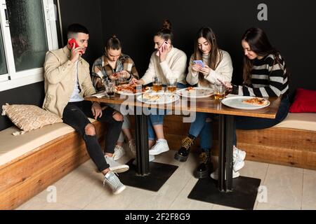 un groupe de jeunes utilisent leur téléphone portable dans une pizzeria Banque D'Images