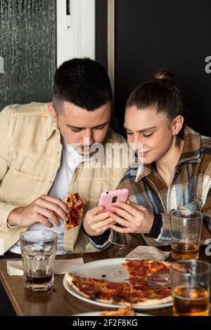 une fille montre à son partenaire un message sur son mobile téléphone pendant qu'ils mangent Banque D'Images