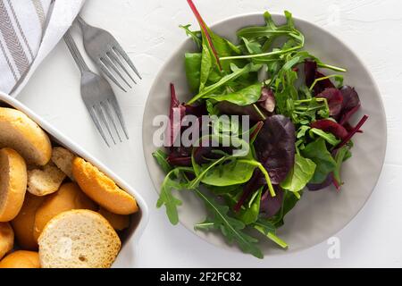 Salade mixte biologique fraîche de feuilles d'arugula, épinards et autres légumes verts dans une assiette, petits pains secs et une assiette de salade, petit déjeuner léger Banque D'Images