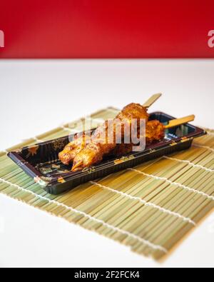 Vue latérale des brochettes de poulet satay à emporter sur un tapis de bambou sur une table blanche et un fond rouge, avec un espace de copie Banque D'Images