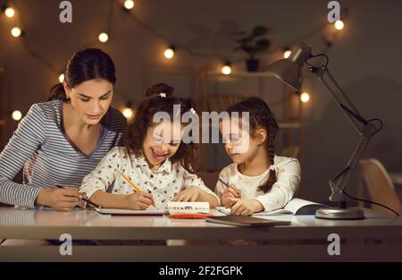 Mère avec des filles qui desseaient sur papier pour faire leurs devoirs à la maison le soir Banque D'Images