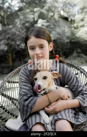 Une fille est assise sur une chaise de jardin avec un chien sur les genoux Banque D'Images