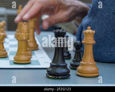 Main de l'homme sur une pièce d'échecs avec d'autres pièces d'échecs assis hors du plateau sur une table. Gros plan. Banque D'Images