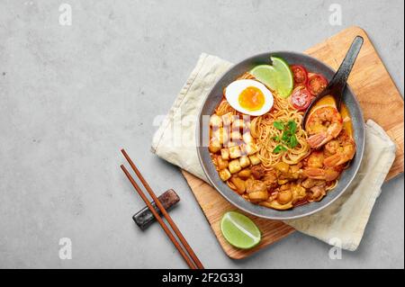 Laksa dans un bol gris sur une table en béton. Soupe de nouilles à la noix de coco avec viande de poulet et crevettes de la cuisine peranakan. Cuisine asiatique. Banque D'Images