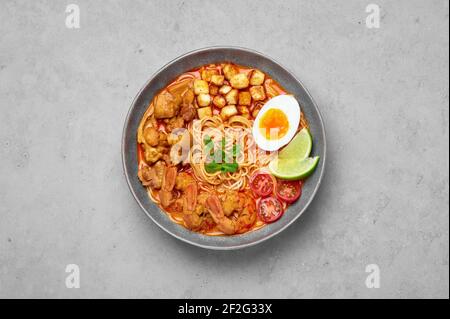 Laksa dans un bol gris sur une table en béton. Soupe de nouilles à la noix de coco avec viande de poulet et crevettes de la cuisine peranakan. Cuisine asiatique. Banque D'Images