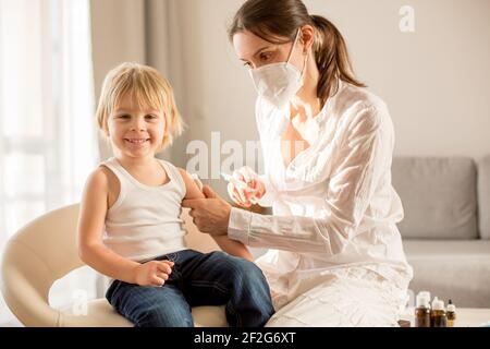 Petit enfant, garçon blond, injection dans la salle de consultation à partir de la pédiatrie, vaccination annuelle. Banque D'Images