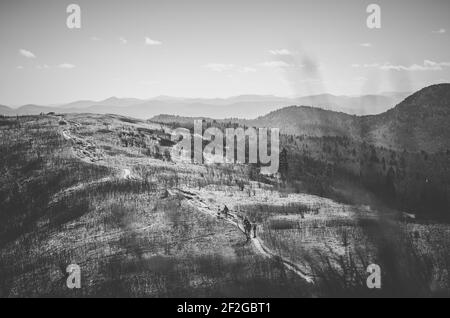 Une photo en niveaux de gris d'un groupe de personnes qui se lever par un sentier pour atteindre le sommet d'une colline en hiver Banque D'Images