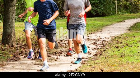 Quatre garçons du secondaire s'entraîner dans une équipe de cross-country qui s'exécute ensemble dans un parc avec des feuilles sur le sol. Banque D'Images