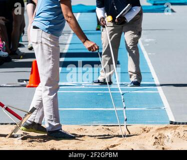 Des officiels de piste mesurant la distance d'un athlète sautent dans la fosse de sable avec une piste bleue à l'extérieur. Banque D'Images