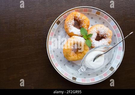 Petit déjeuner. Beignets sur l'assiette. Trois beignets savoureux avec sucre en poudre, feuille de menthe verte et crème sure sur l'assiette. Arrière-plan en bois avec espace de copie Banque D'Images