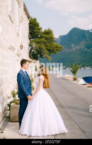 Le marié et la mariée tiennent les mains et regardent les uns les autres sur la toile de fond d'une belle maison blanche Dans Perast Banque D'Images