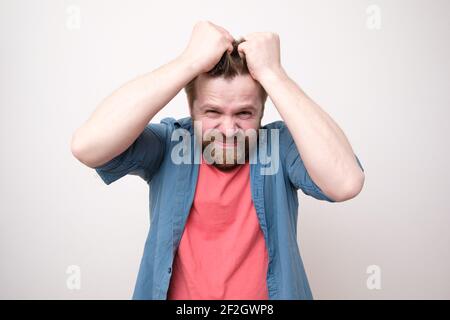 Homme caucasien en stress, il est nerveux, tenant les cheveux avec les mains et regardant la caméra. Arrière-plan blanc. Banque D'Images