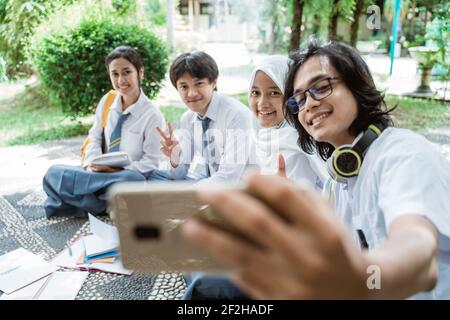 ensemble des élèves du secondaire souriant lorsqu'un groupe est en train de se faire un selfie d'amis se sont assis sur le sol Banque D'Images