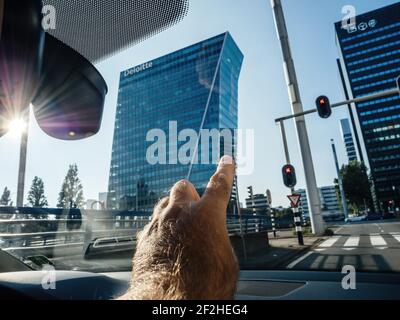 Main mâle de POV pointant de la fenêtre de la voiture à la Grands gratte-ciel avec Deloitte Audit Big four dans le siège social Capitale néerlandaise - visite de la Haye Banque D'Images