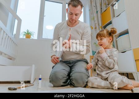 Une petite fille de 4 ans aide son père à assembler ou à fixer le tiroir du lit dans la chambre des enfants. Banque D'Images