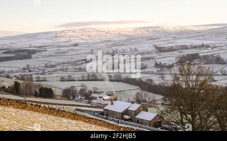 La lumière du soleil en fin d'après-midi capture les sommets des collines enneigées de Weardale, les Pennines du Nord, comté de Durham, Royaume-Uni. Une cheminée fume d'une maison en pierre Banque D'Images