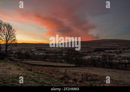 Une vue sur les Pennines du Nord (Weardale, comté de Durham, Royaume-Uni) en hiver; un lever de soleil rose / orange remplit le ciel. Banque D'Images