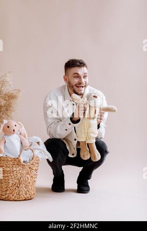 Joyeux homme positif avec la barbe en chemise blanche tenant l'ours en peluche, préparant le présent pour sa petite fille. Panier de paille avec de nombreux jouets goujon intérieur Banque D'Images