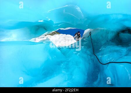 Vue à travers le tunnel de glace bleu sur le grimpeur explorant la beauté de Fox Glacier, South Island, Nouvelle-Zélande. Adrénaline et aventure concept. Banque D'Images