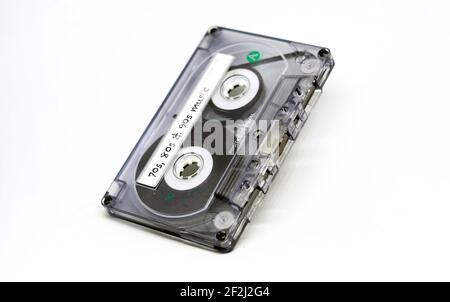 cassette audio transparente avec musique des années 70, 80 et 90 inscrite sur l'étiquette adhésive. Technologie obsolète isolée sur fond blanc. Ana Banque D'Images
