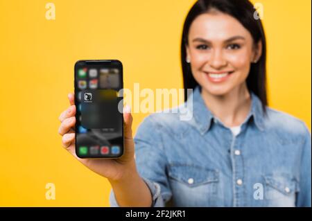 Kiev, Ukraine - 28 février 2021. Une fille défocused tient un smartphone avec l'icône d'une application Clubhouse sur l'écran de l'iPhone sur un arrière-plan isolé. Application pour une communication vocale des personnes Banque D'Images