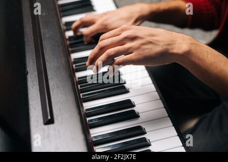 Gros plan des mains d'un homme méconnaissable jouant au piano dans un studio d'enregistrement à domicile. Banque D'Images