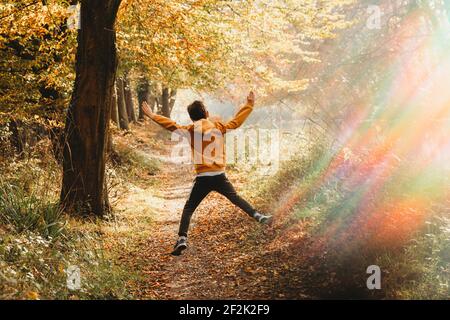 Garçon bondissant dans l'air sur le chemin sous l'arbre avec arc-en-ciel Banque D'Images