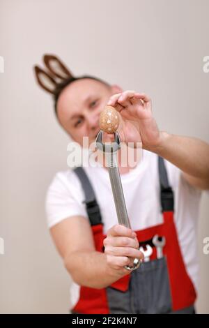 Vacances de Pâques, concept de célébration. Travailleur ou mécanicien souriant drôle porte des oreilles de lapin sur la tête, tenant des clés et peint blanc d'oeuf Banque D'Images