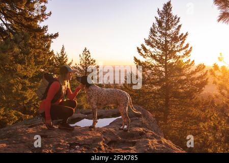 Vue latérale d'une jeune femme en randonnée avec un chien sur la montagne au coucher du soleil Banque D'Images