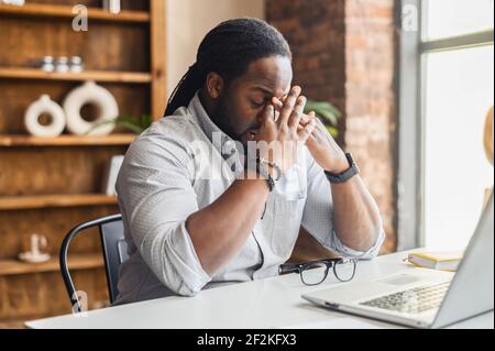 Un homme d'affaires afro-américain frustré qui se préoccupe du projet, assis à son bureau avec un ordinateur portable au travail, un employé noir déprimé se sent stressé par erreur ou par erreur inattendue d'ordinateur crash Banque D'Images