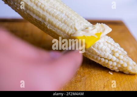 Étaler la mayonnaise à la main sur le maïs au-dessus de la planche à découper en bois Banque D'Images