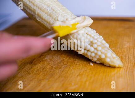 Étaler la mayonnaise à la main sur le maïs au-dessus de la planche à découper en bois Banque D'Images