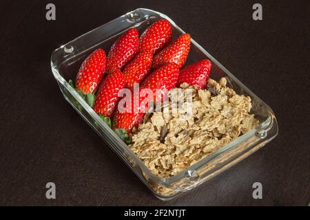 Élégant plat en verre rempli de fraises sauvages et de grains entiers avec chocolat noir sur une table en bois noir. Alimentation avec des fruits et des céréales. Banque D'Images
