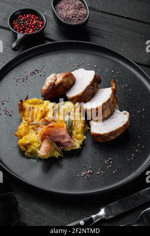 Filet de porc grillé et purée de pommes de terre gratin avec sauge et prosciutto, sur plat, sur fond de table en bois noir Banque D'Images