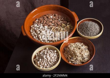 Un grand pot d'argile artisanale avec des amandes, des pistaches et des noix, ainsi que trois bols remplis de lentilles, de pois chiches et de flocons de riz grillés. Banque D'Images