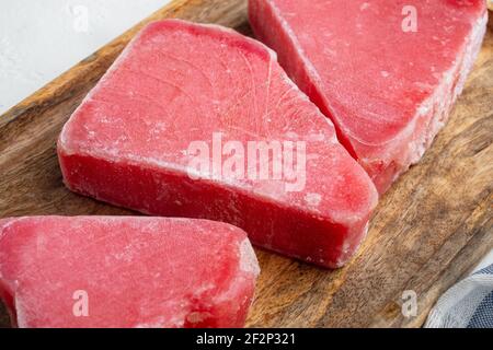 Ensemble de steaks de thon surgelé, sur plateau en bois, sur fond de pierre blanche Banque D'Images