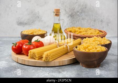 Variété de pâtes crues avec œufs, tomates fraîches et bouteille d'huile Banque D'Images