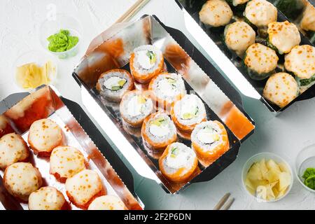 De savoureux petits pains à sushis dans des boîtes jetables, sur fond de pierre blanche Banque D'Images