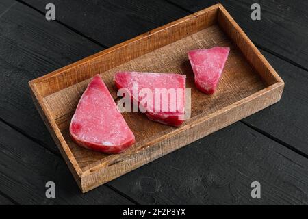 Ensemble de steaks de thon surgelé, dans une boîte en bois, sur fond en bois noir Banque D'Images