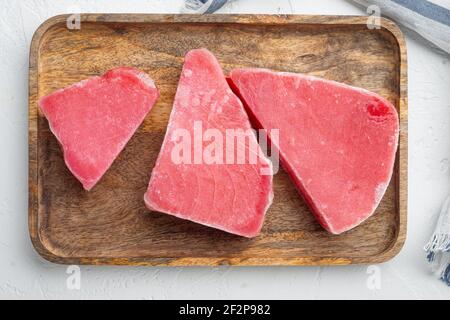 Ensemble de steaks de thon surgelé, sur plateau en bois, sur fond de pierre blanche, plan de dessus Banque D'Images