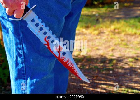Un énorme couteau de Bowie avec du sang qui descend la lame dans une main masculine; crime violent ou concept de terrorisme Banque D'Images
