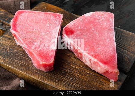 Ensemble de steaks de thon surgelé, sur planche à découper en bois, sur fond de table en bois foncé Banque D'Images