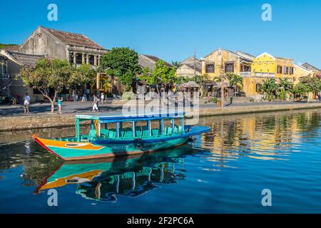 Une vue magnifique sur un bateau de pêche multicolore et des bâtiments de couleur pastel jaune qui se reflètent dans la rivière Thu bon à Hoi an Old Town, Vietnam Banque D'Images