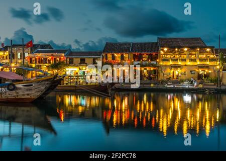 Une vue en soirée des restaurants de bateaux de pêche et des bâtiments de restaurants éclairés se reflétant dans la rivière Thu bon à Hoi an Old Town, Vietnam Banque D'Images