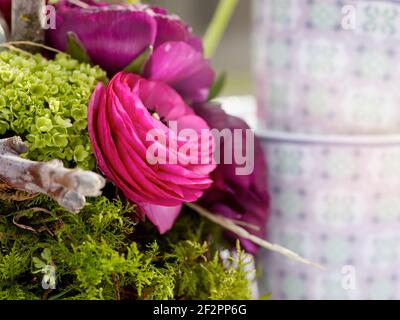 Gros plan d'un arrangement floral de Pâques avec des fleurs de ranunculus roses, des oeufs de Pâques, des oeufs de caille et des plumes, en arrière-plan une tasse de café Banque D'Images