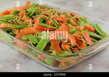 Pois mange-tout crus et pelures de carottes et cocotte de pâtes cuites couches pour la cuisson dans une plaque de cuisson en verre Banque D'Images