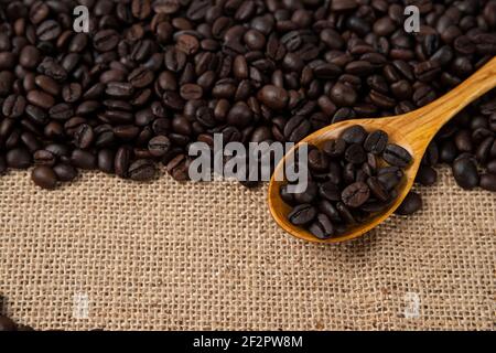 Pile de grains de café torréfiés moyens avec une cuillère en bois parsemée en toile de jute Banque D'Images