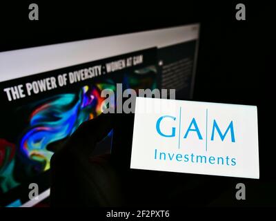 Personne détenant un smartphone avec le logo de la société suisse de services financiers GAM Investments sur écran devant le site Web. Mise au point sur l'affichage du téléphone. Banque D'Images