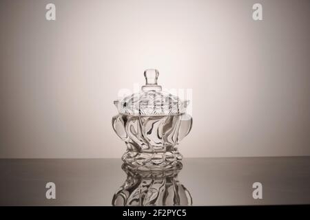 Videz le bol en verre avec un couvercle et son reflet un arrière-plan gris Banque D'Images